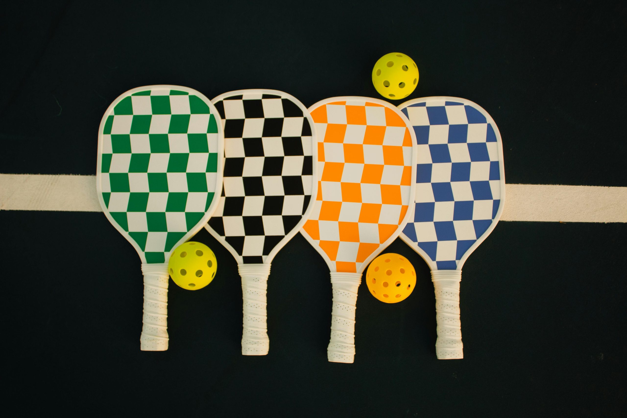 Cuatro palas de pickleball con diseño de damero sobre una pista